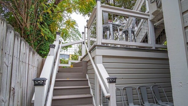 A staircase with a wooden handrail and a metal railing, leading to a deck area with chairs.