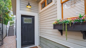 A house with a black front door, a small porch with a brick floor, and a window with a flower box.
