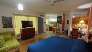 Une chambre d’hôtel comprenant un lit, un canapé vert, une télévision, un coin cuisine et une table à manger.