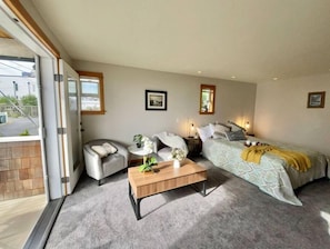 A modern bedroom with a bed, two chairs, a small table, and a window.