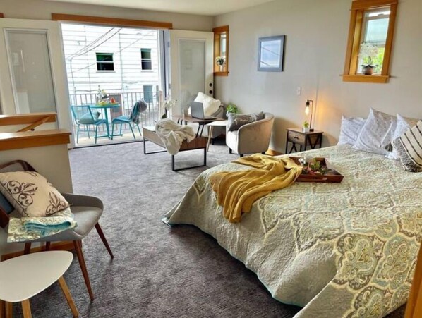 A hotel room with a bed, a desk, a chair, and a small balcony.
