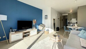 A modern living room with a flat-screen TV, a sofa, a coffee table, and a dining area with chairs.
