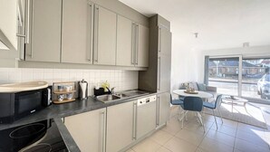 A modern kitchen with grey cabinets, a black microwave, and a dining area with a table and chairs.