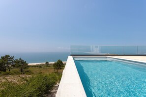 Une piscine offrant une vue dégagée sur la mer, avec un bâtiment moderne en arrière-plan.