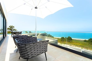 A balcony with a view of the sea, furnished with chairs and a table, and an umbrella.