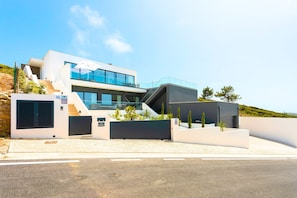 A modern two-story building with a flat roof, large windows, and a staircase leading to the upper level.