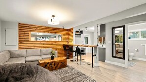 Ein modernes Wohnzimmer mit grauem Sofa, einer Wand als Holzoptik, einem Couchtisch und einem gemusterten Teppich.