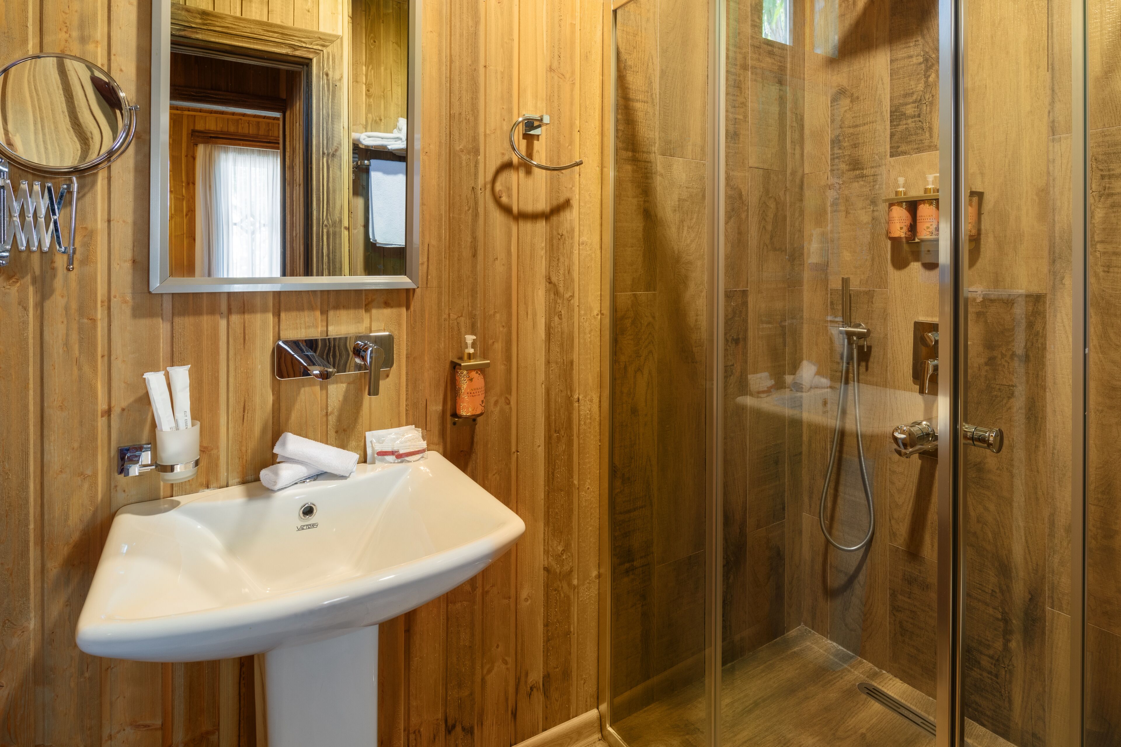 Bagno con parete in legno, lavandino bianco, specchio e cabina doccia in vetro.