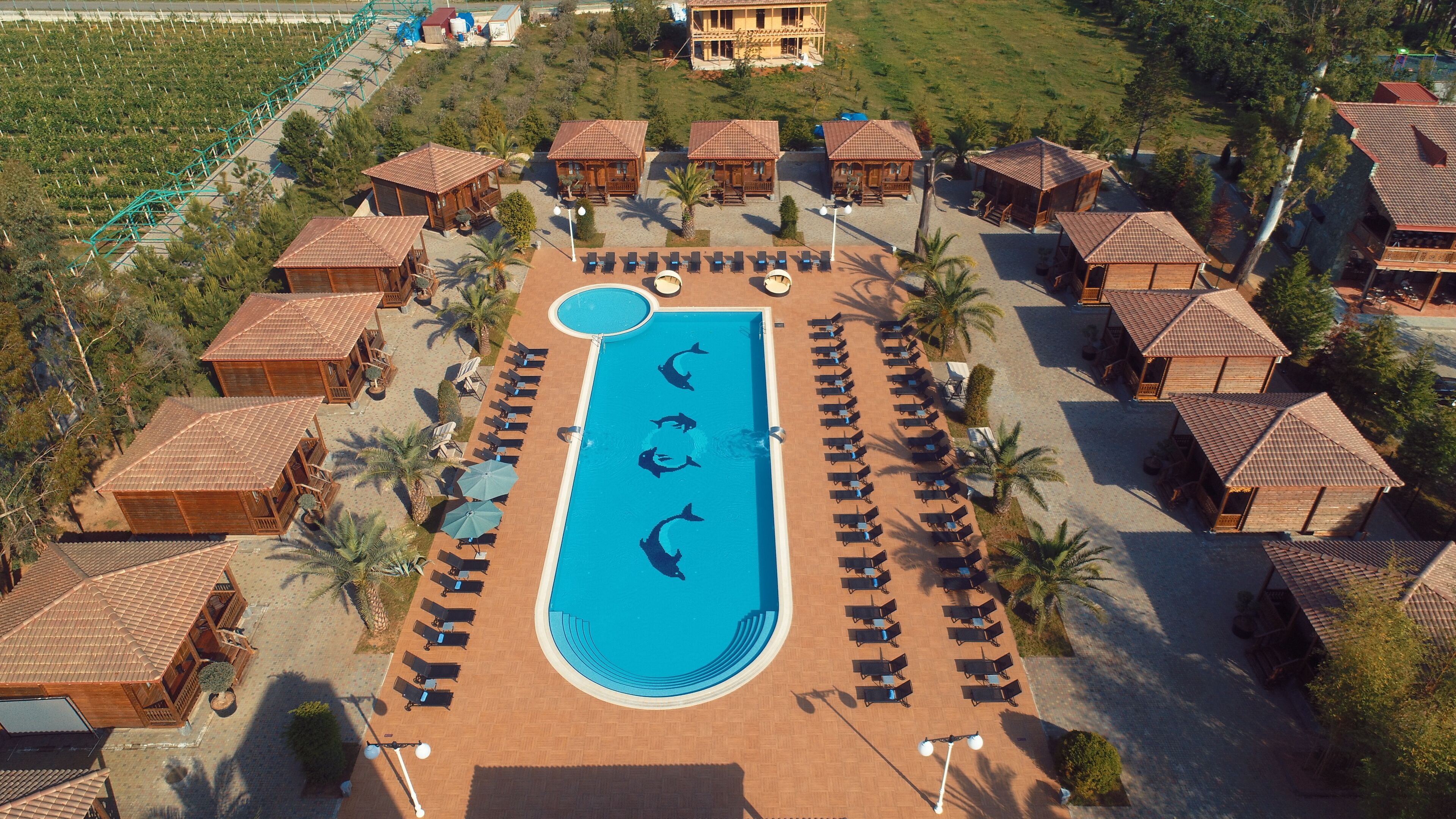 An aerial view of a resort with a central swimming pool, multiple wooden villas, and a well-maintained garden area.