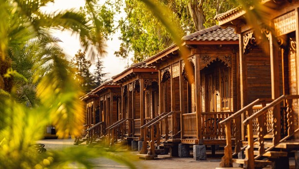 A row of traditional wooden buildings with intricate designs, a central staircase, and a pathway leading through them. - Chateau Kvirike (Kobuleti)