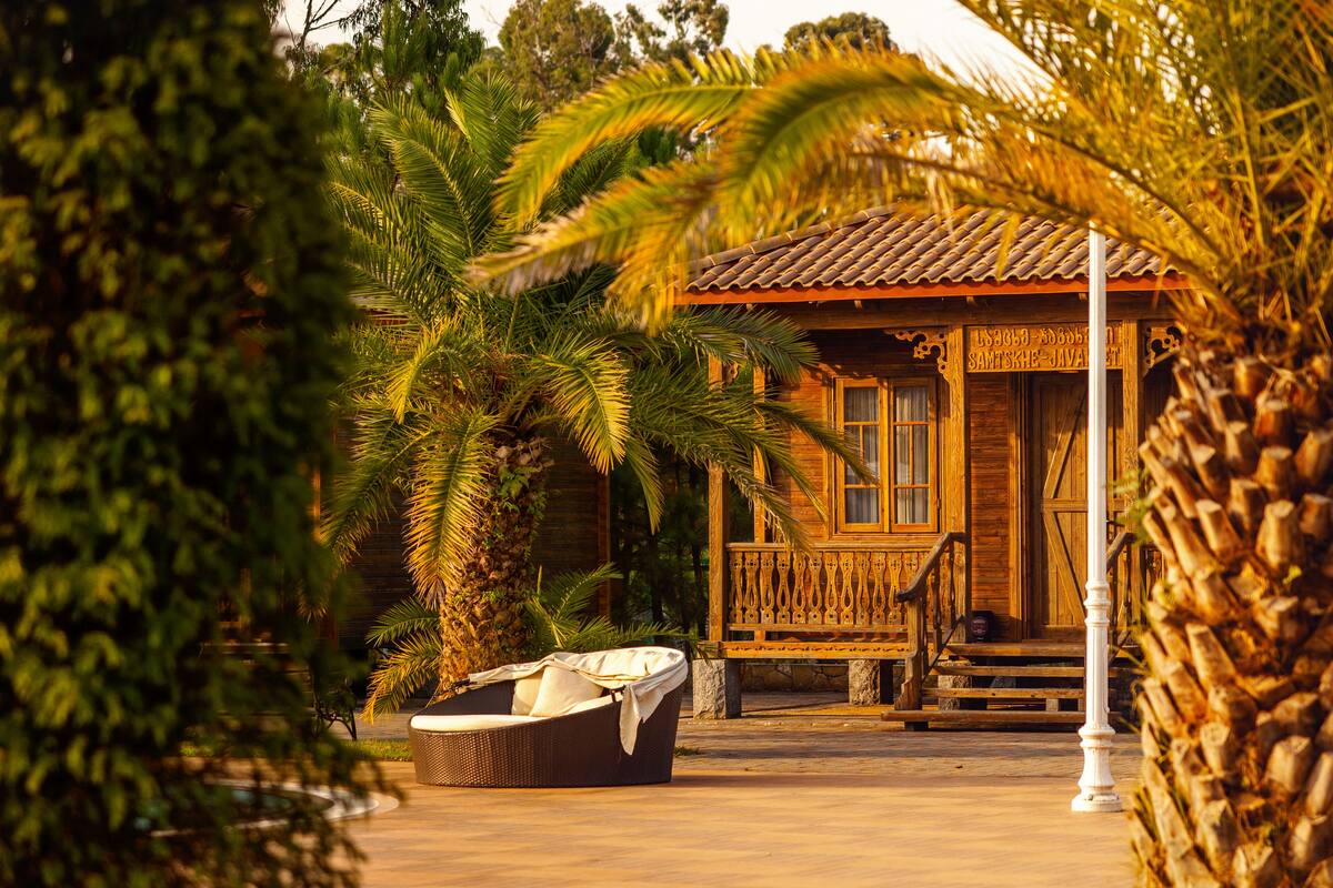 A wooden building with a tiled roof, surrounded by palm trees and a wicker chair.
