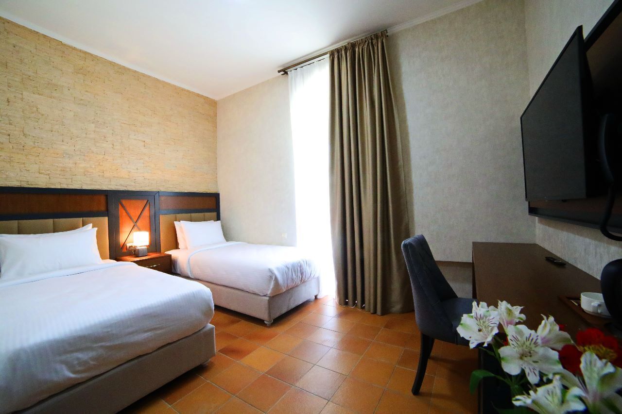 A hotel room with two beds, a desk, a chair, a TV, and a window with curtains.
