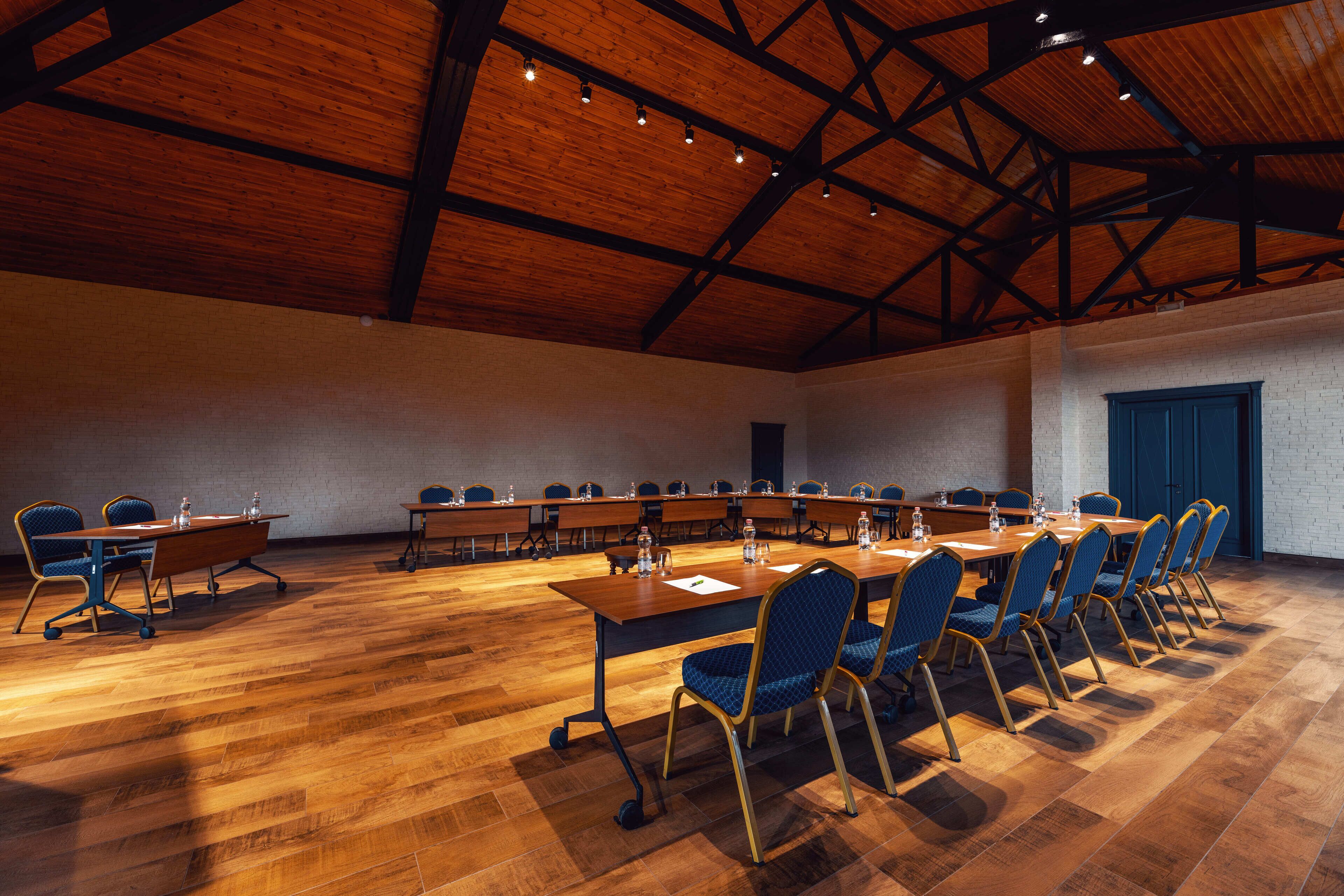 Un salón de conferencias con una mesa larga y sillas, pisos de madera y un techo alto con vigas a la vista.