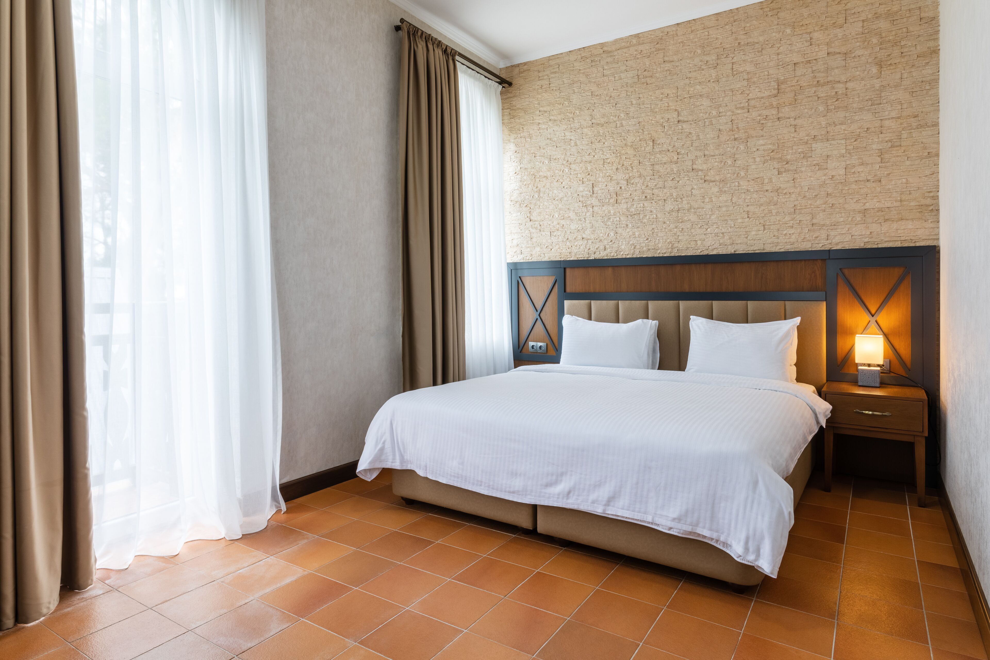 A hotel room with a bed, a nightstand, a lamp, and a brick wall.