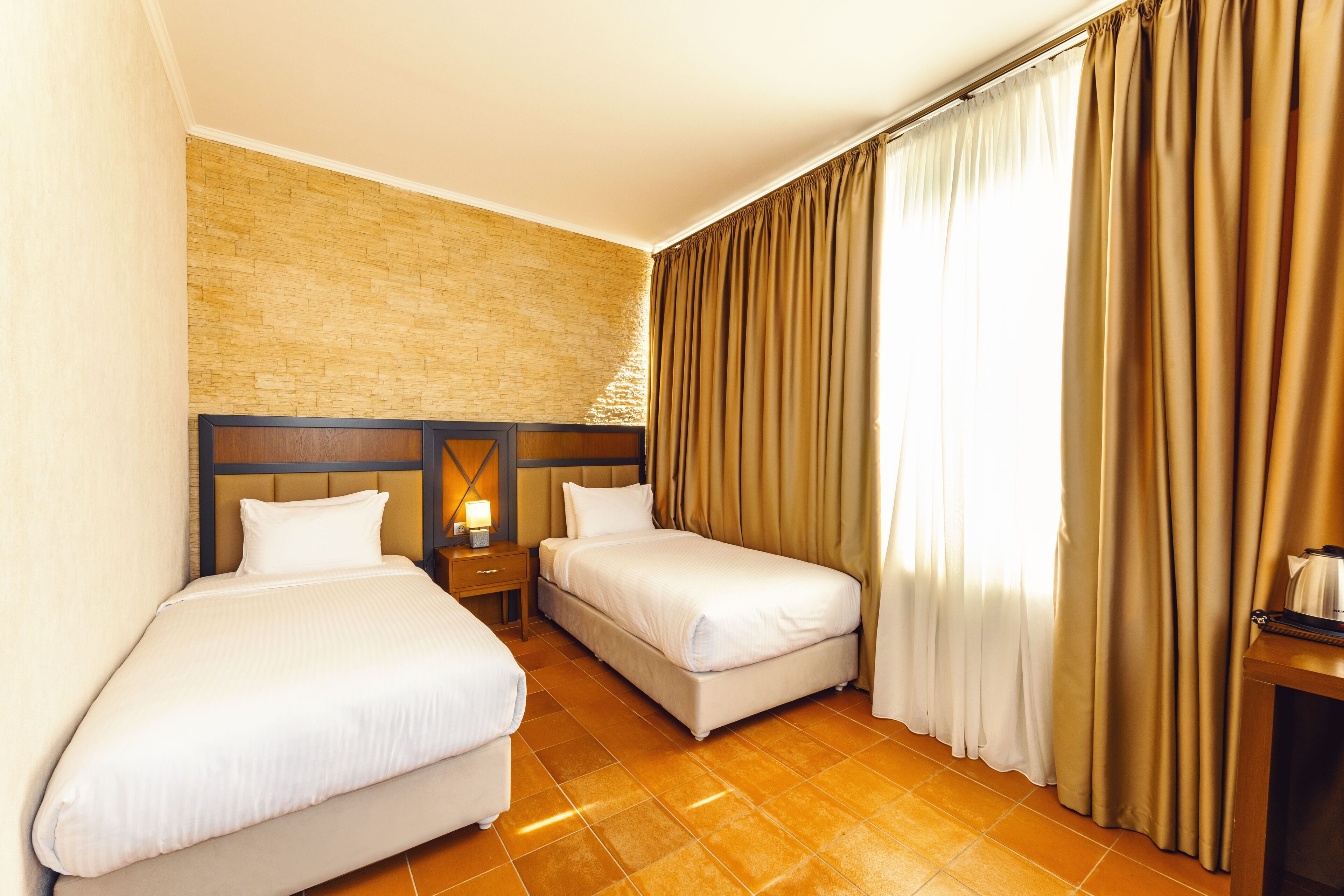 A hotel room with two beds, a brick wall, and a large window with curtains.