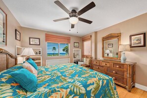Quarto com cama, ventoinha no teto, cômoda, espelho e janela com vista para o mar.