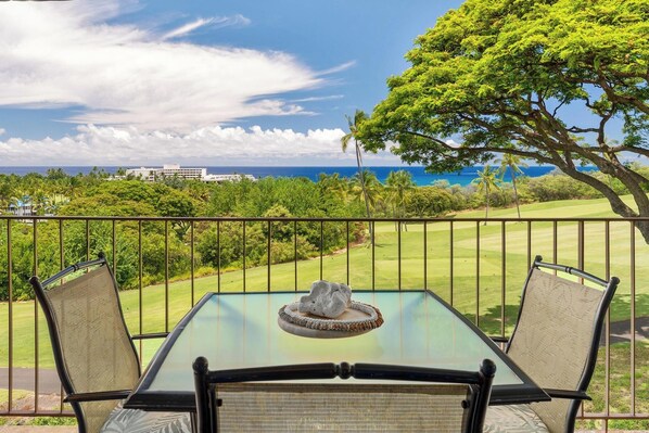 A balcony with a table and chairs, overlooking a golf course and ocean view. - Keauhou Akahi Ocean View Condo Overlooking Kona Country Club Golf Course (Kailua-Kona)