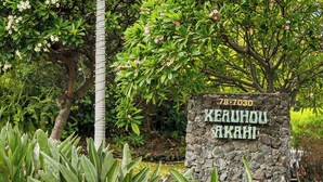 A stone sign with 'KEAUHOU AKAHI' and a number '78-7030' in a lush garden setting.