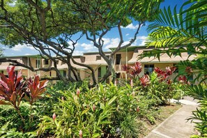 A hotel with multiple-story buildings, a garden with various plants, and a clear blue sky. - Keauhou Akahi Ocean View Condo Overlooking Kona Country Club Golf Course (Kailua-Kona)