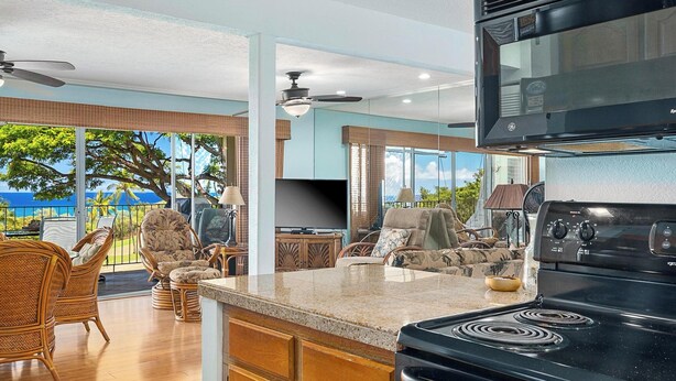 A modern kitchen with a built-in stove, large windows, wicker furniture, and a view of the outdoors.