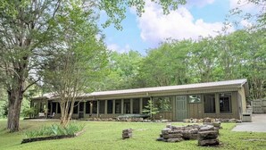 Un bâtiment d’un seul étage, doté d’un porche couvert, entouré d’une cour verdoyante et d’arbres.