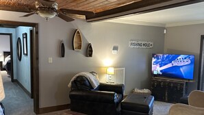 Un salon chaleureux avec un ventilateur de plafond, un canapé en cuir, une table basse en bois et un téléviseur.