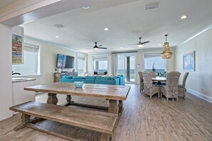 A spacious kitchen with a large wooden table, a blue sofa, wicker chairs, and a view of the ocean.