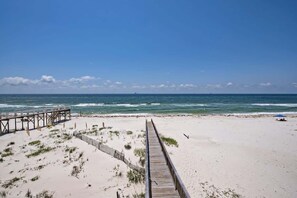 A beach with a wooden boardwalk leading to the water, sandy dunes, and a clear blue sky.