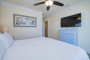 A bedroom with a large bed, a ceiling fan, a flat-screen TV, and a dresser.
