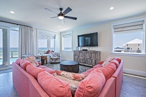 A spacious living room with a large sofa, a television, and a view of the ocean.