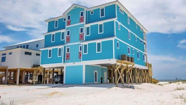 Een meerhoog gebouw met een blauwe gevel, een overdekte ingang en een zandstrand op de achtergrond.