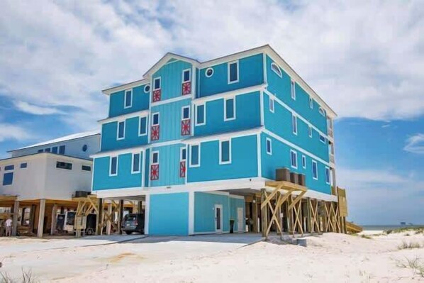 A multi-story building with a blue exterior, a covered entrance, and a sandy beach in the background.