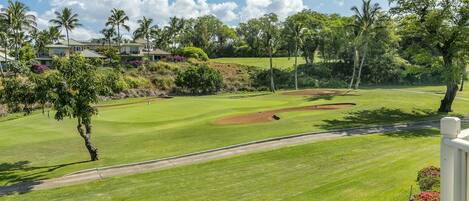 A golf course with well-maintained grass, sand bunkers, and a clear sky.