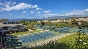 Complejo de canchas de tenis con varias pistas, rodeado de vegetación exuberante y vista al océano.
