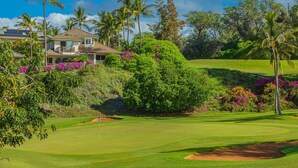 Un campo de golf con una casa al fondo, rodeado de exuberante vegetación y palmeras.