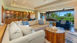 A spacious living room with a large beige sectional sofa, a wooden coffee table, and a view of the outdoor patio area with a blue sofa and chairs.