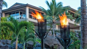 A resort with two lit torches, a waterfall, and a modern building with balconies.