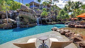 A poolside area with a waterfall, lounge chairs, and a view of a resort building.