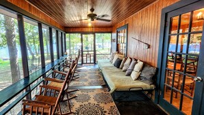 A covered outdoor seating area with wooden benches and a sofa, large windows, and a ceiling fan. - Roddy's Roost Lakefront Cabin - Hot Springs AR
 (Hot Springs)