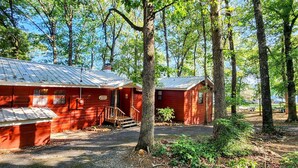 A rustic cabin with a metal roof, surrounded by tall trees and a gravel driveway. - Roddy's Roost Lakefront Cabin - Hot Springs AR
 (Hot Springs)