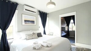 Une chambre d’hôtel avec un grand lit, un tableau au mur et une vue sur l’extérieur par une porte ouverte.