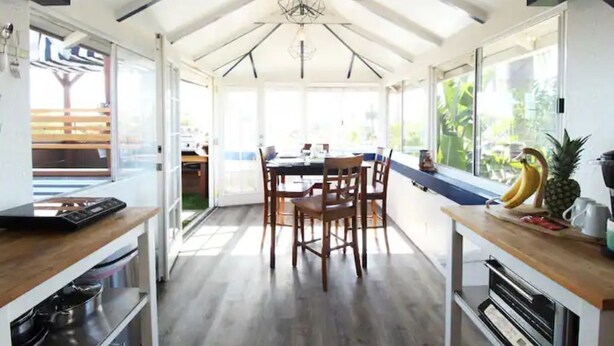 Une cuisine moderne avec des meubles en bois, un coin repas comprenant une table et des chaises, et une grande fenêtre laissant entrer la lumière naturelle.