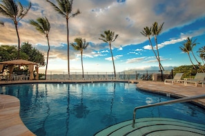 A swimming pool with lounge chairs and palm trees, surrounded by a fence. - Oceanfront Wailea condo w/ pool, lanai and snorkeling (Wailea)