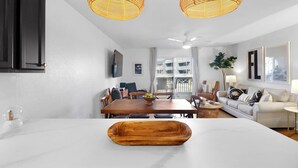 A modern kitchen with a marble countertop, wooden dining table, and two wicker pendant lights.