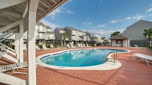 A swimming pool with lounge chairs, a covered area, and residential buildings in the background.