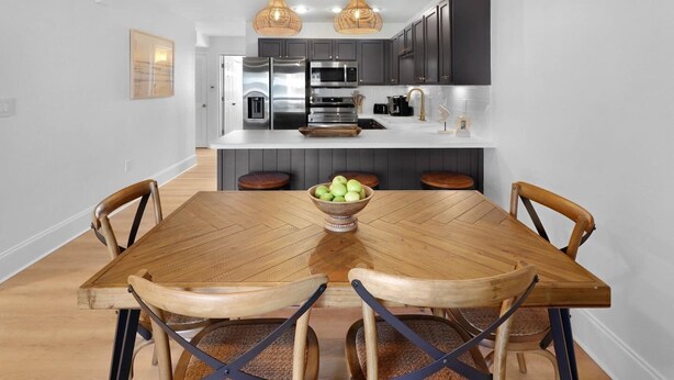 A modern kitchen with dark cabinets, a stainless steel refrigerator, and a wooden dining table with chairs.