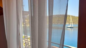 A window with sheer curtains, a view of a calm sea, and a sailboat in the distance. - Sponga 2 Apartment with balcony and sea view (Polače)