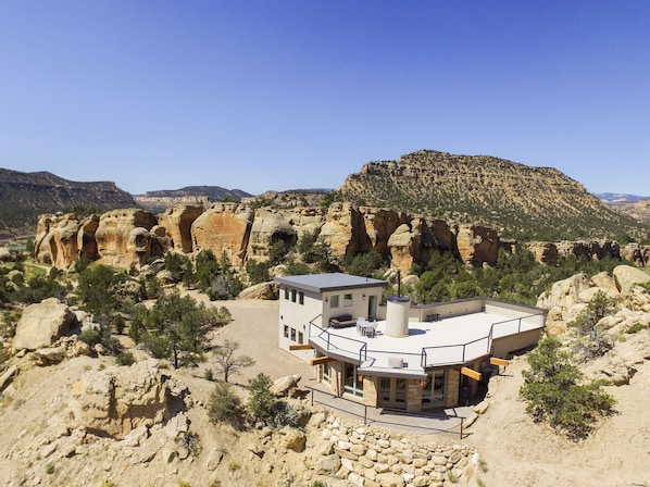 A modern building with a flat roof and large windows, surrounded by rocky terrain and sparse vegetation.