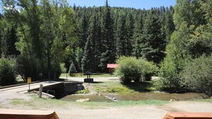 A wooden deck overlooking a forested area with a small bridge and a red building. - Located on the river, facing the Mountains (Red River)