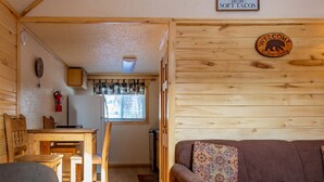 A cabin interior with a wooden dining table, a sofa, a patterned pillow, a welcome sign, and a fire extinguisher. - Located on the river, facing the Mountains (Red River)